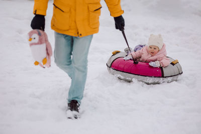 Dad rides little girl on sled for walk in winter snowy day.