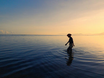 Woman standing in sea during sunset