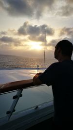 Man fishing in sea against sky during sunset