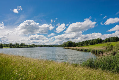 Scenic view of river against cloudy sky on sunny day