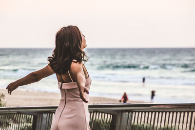 Rear view of woman standing at beach against clear sky