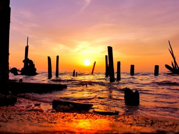 Silhouette wooden posts in sea against sky during sunset