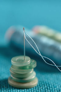 Close-up of sewing needle with button and thread spools on table