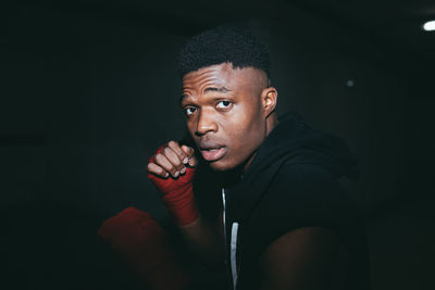 Young strong african american sportsman in boxing hand wraps working out and looking at camera in building