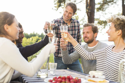 Group of happy friends toasting beer glasses during lunch at picnic table