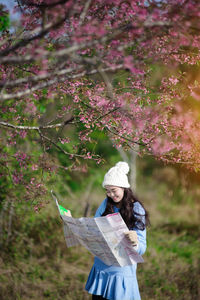 Smiling woman looking at paper while standing under tree