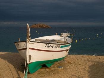 Boat moored on beach against cloudy sky