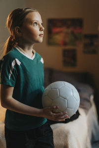 Elementary girl with soccer ball day dreaming while standing in bedroom