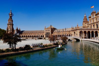 View of canal in city against clear blue sky