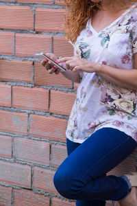 Midsection of woman holding umbrella while standing against wall