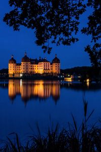 Illuminated buildings by lake against sky at night