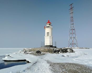 Lighthouse by sea against clear sky