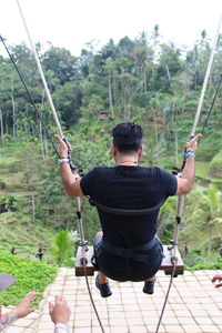 Rear view of man holding rope against trees