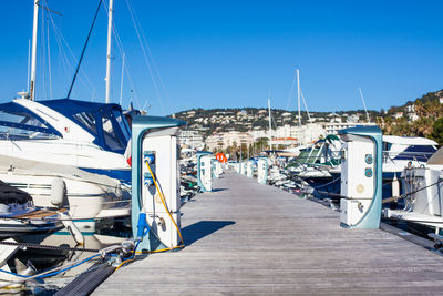 Boats moored at harbor against clear blue sky