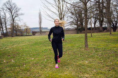 Full length of mature woman jogging on grassy field
