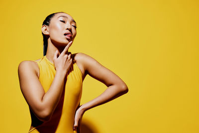 Portrait of young woman standing against yellow background