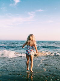 Rear view of young woman standing at beach against sky