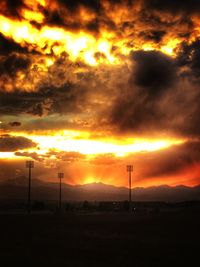 Silhouette trees on field against dramatic sky during sunset