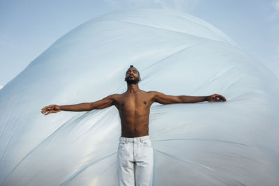 Shirtless man with arms outstretched standing in front of foil