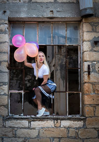 Happy woman having fun holding colorful air balloons on a broken window