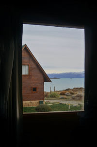 House on field against sky seen through window