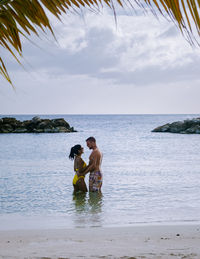 Couple embracing while standing at shore against sky