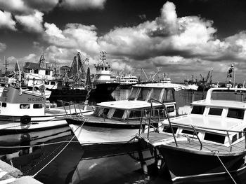 Boats moored at harbor against cloudy sky