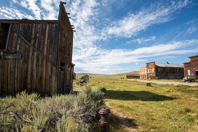 Abandoned wooden built structure in ghost town on field against sky