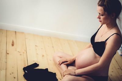 Pregnant woman with baby clothing sitting on hardwood floor