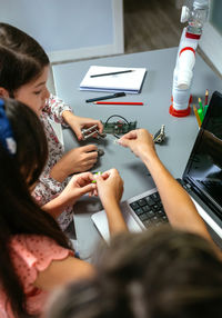 Female teacher helping girl students to assemble pieces of machine in a robotics class