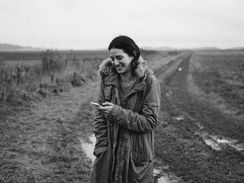 Smiling woman using cell phone on field road