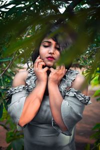 Portrait of woman standing by tree against plants