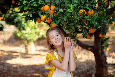 Portrait of young woman standing against tree