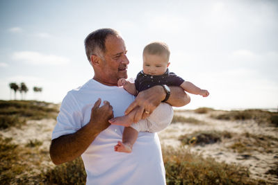 Grandfather holding grandson while standing on beach