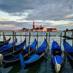 Gondola boats moored by wooden posts in grand canal against cloudy sky during sunset