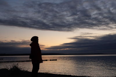 Silhouette man standing at beach against sky during sunset