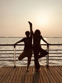 Silhouette friends standing on pier against sea during sunset