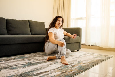 Portrait of young woman sitting by sofa at home