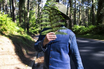 Portrait of a man with a hat and texan clothes covering his face with a fern leaf. fashion concept