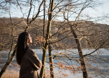 Side view of woman standing by bare trees