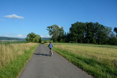 Boy riding bicycle on road amidst field against sky