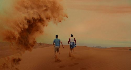 Rear view of two men running on sand dune