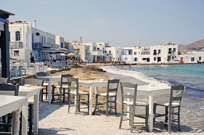 Chairs and table by buildings in city against clear sky