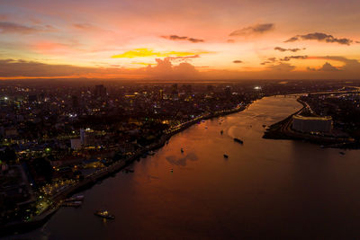 High angle view of illuminated buildings by river against sky during sunset