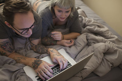 Young couple lying in bed looking at a laptop