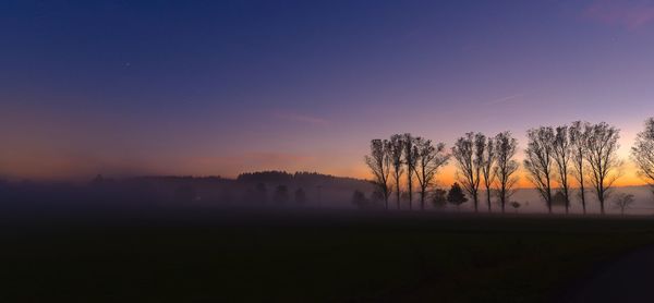 Silhouette trees on field against sky during sunset