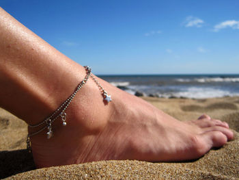 Low section of woman wearing anklet at beach against sky