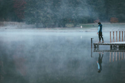 Side view of man standing by lake on jetty during foggy weather