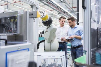 Two men with tablet examining assembly robot in factory shop floor