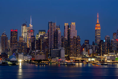 View of illuminated buildings by lake in city against clear sky at night